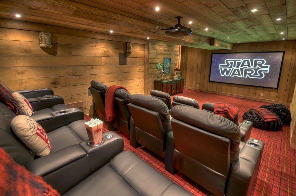 Cozy home theater with recliners, plaid carpet, wood-paneled walls, and a Star Wars screen.