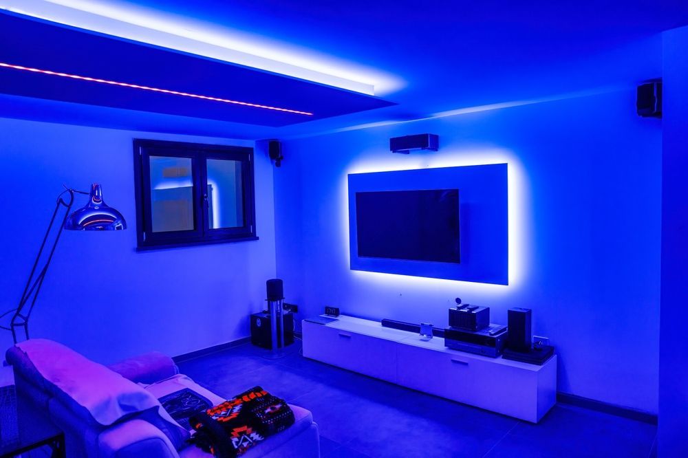 Blue-lit modern living room with wall-mounted TV, sofa, and floor lamp