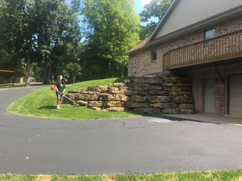 A man is blowing grass in front of a large brick house.