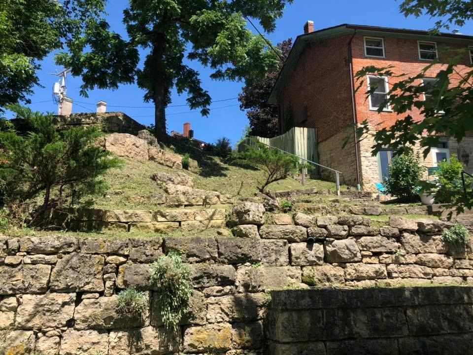 A brick house is sitting on top of a hill next to a stone wall.