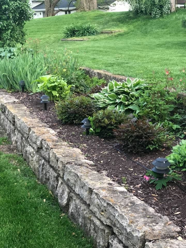 A stone wall surrounds a garden with lots of plants and lights.