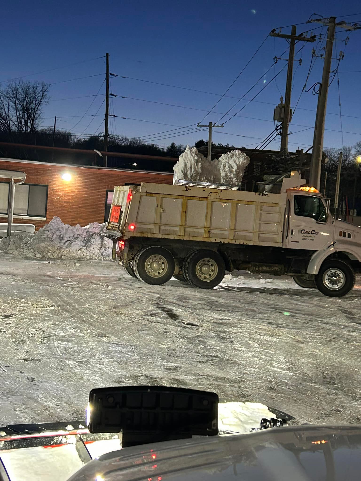 A dump truck is driving through a snowy parking lot at night.