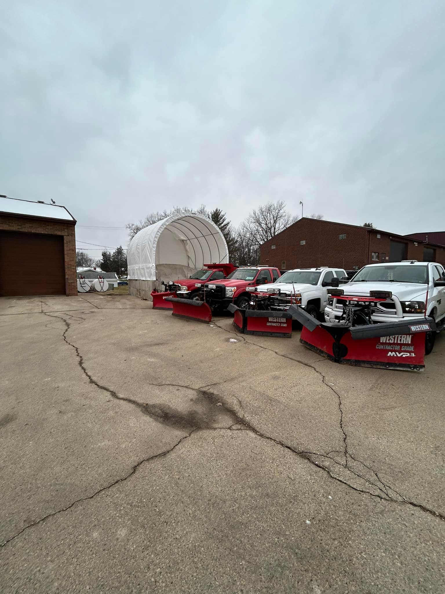 A row of snow plows are parked in a parking lot.