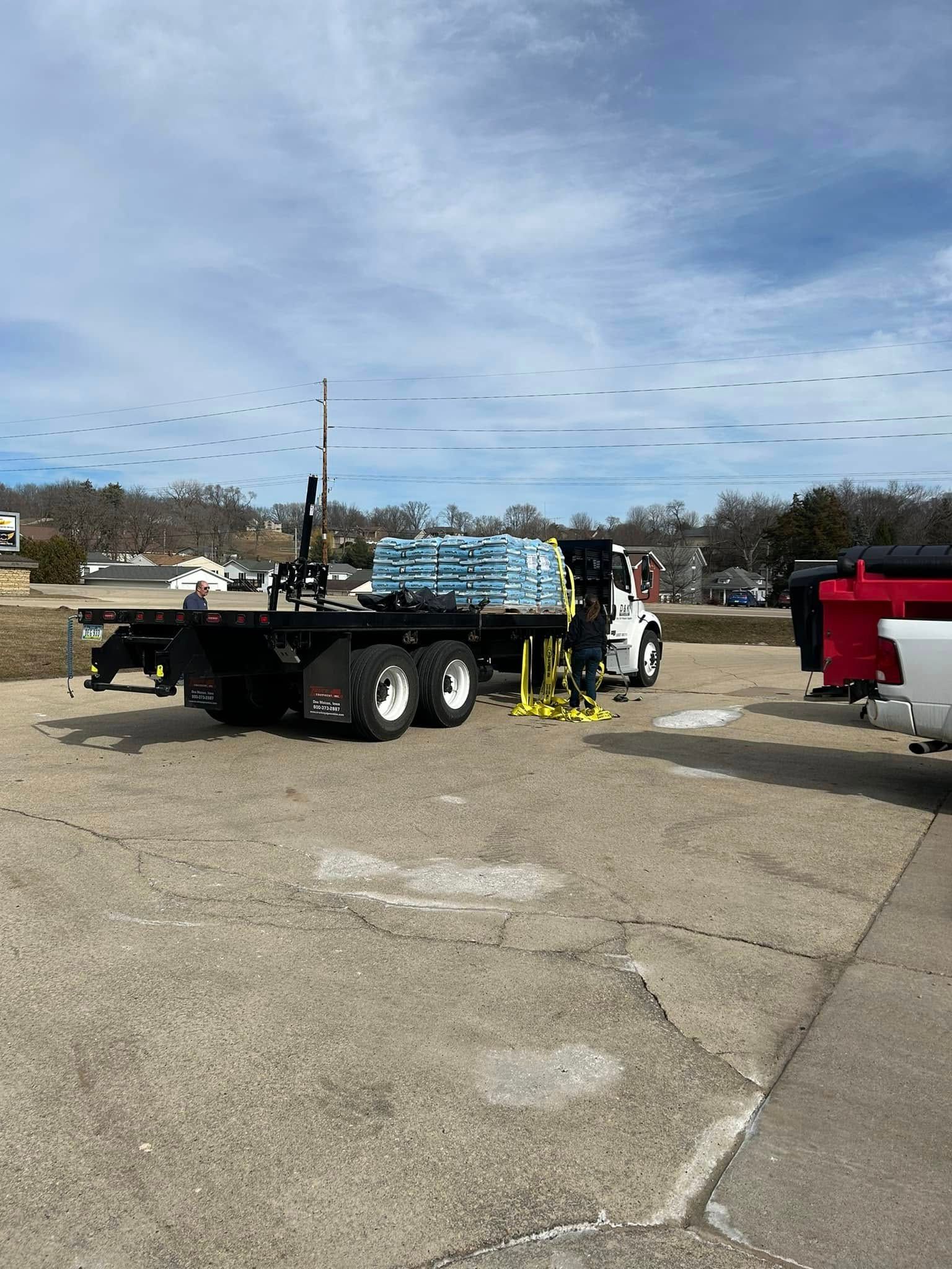 A flatbed truck is parked in a parking lot next to a red truck.