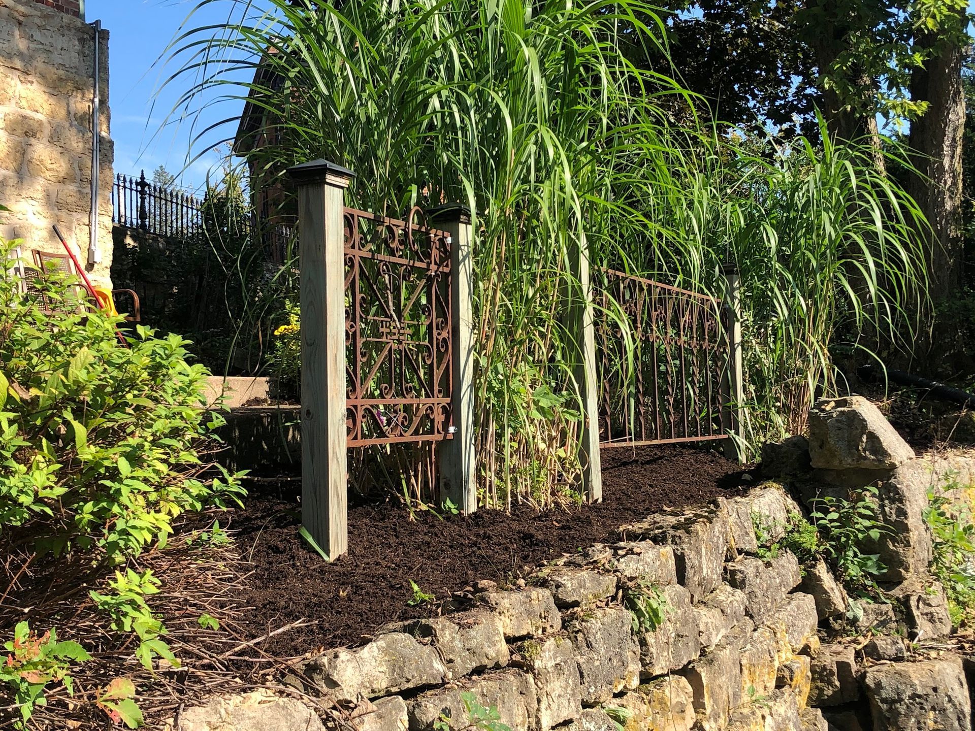 A stone wall is surrounded by tall grass and a fence.