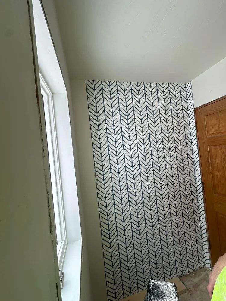 A person is standing in front of a wall with a herringbone pattern on it.