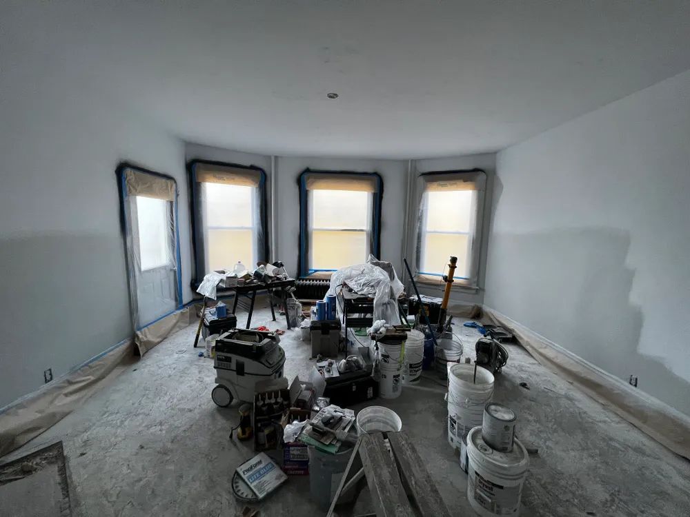 A room with a lot of buckets of paint and tools on the floor.