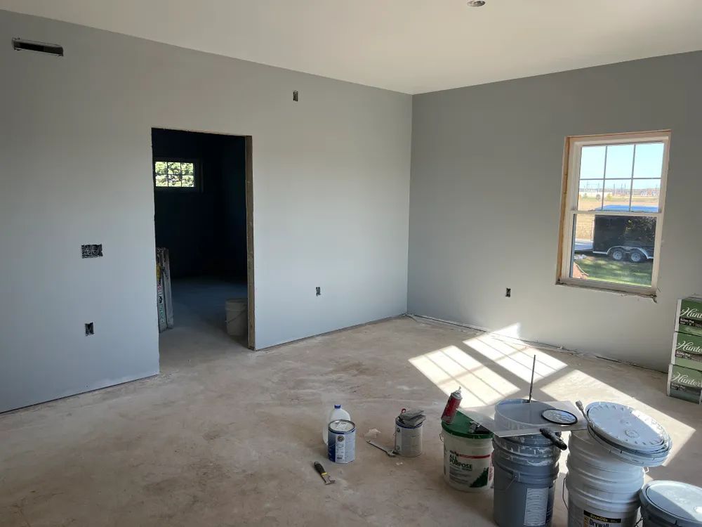 A room with buckets of paint on the floor and a window.