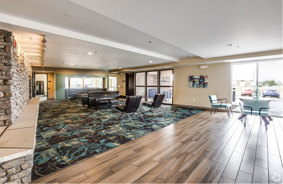 A large lobby with wooden floors , chairs , tables and a fireplace.