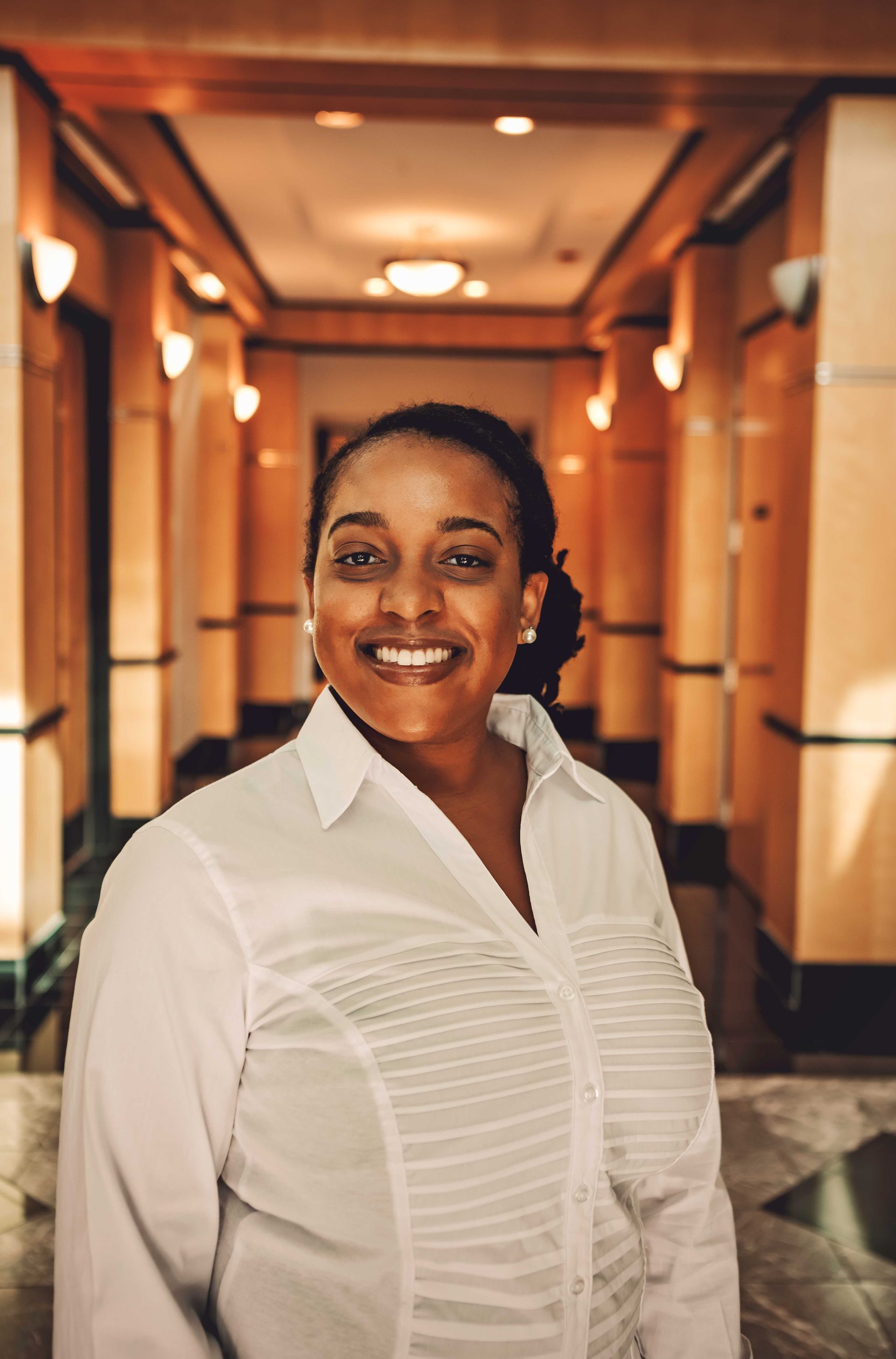 A woman in a white shirt is smiling in a hallway.