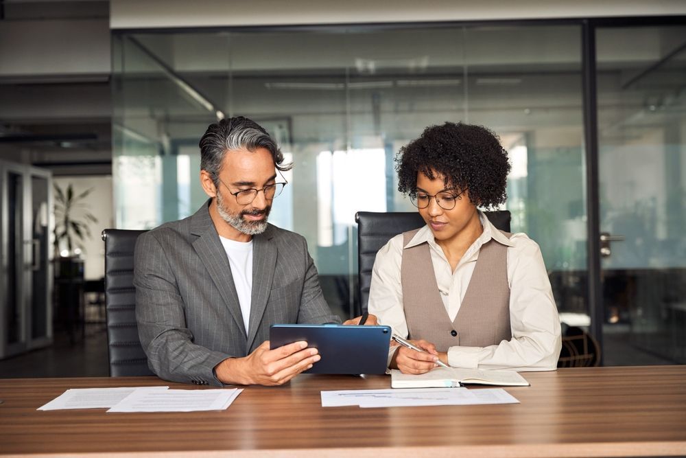 Two coworkers reviewing a tablet at a conference table in a glass-walled office