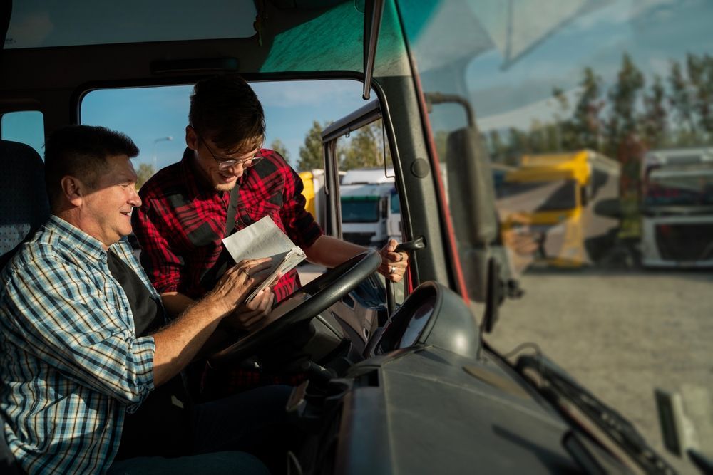 Two workers smiling inside a truck cab, reviewing a document at a construction site.
