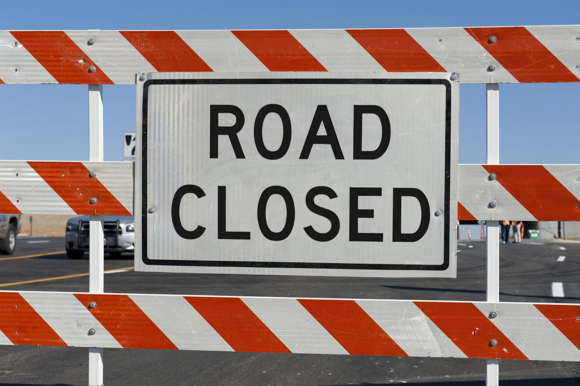 A road closed sign is behind an orange and white barricade