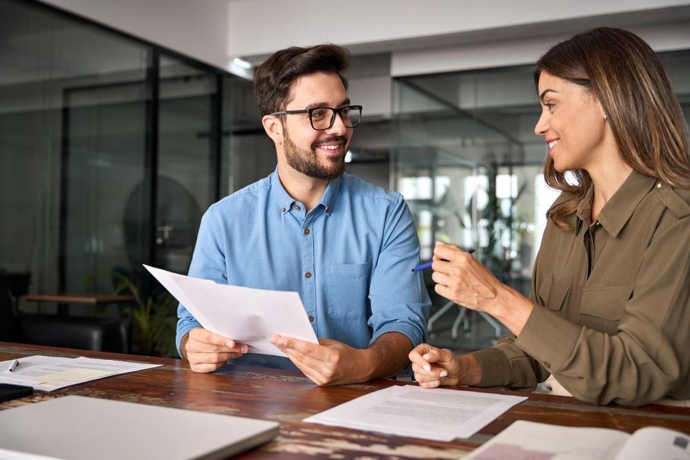 Two coworkers reviewing papers and discussing ideas at a desk in a modern office
