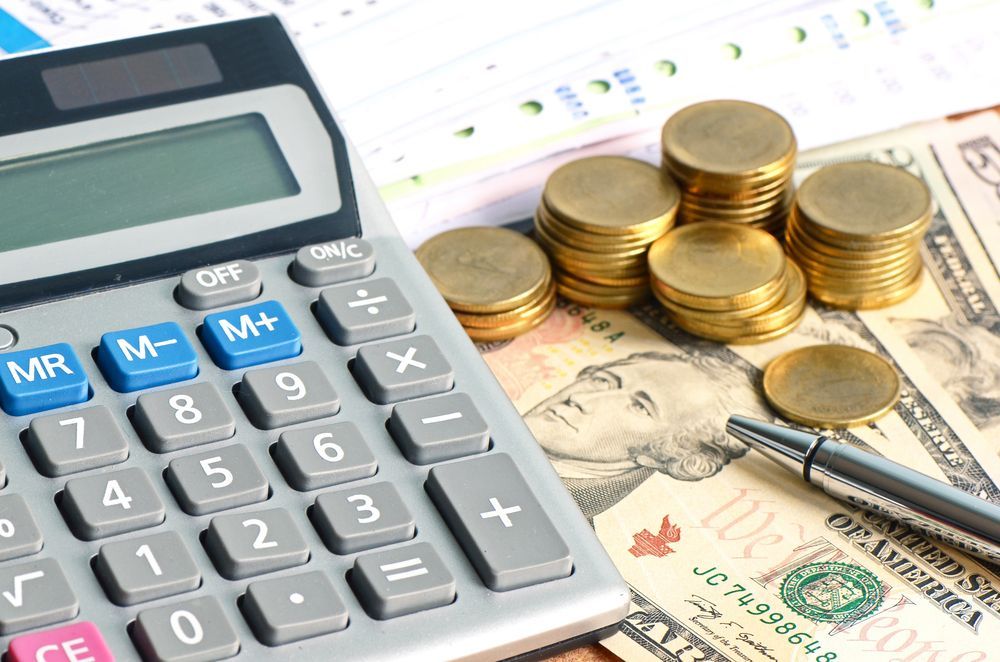 Calculator, coins, money, and a pen on a desk, representing finance and accounting.