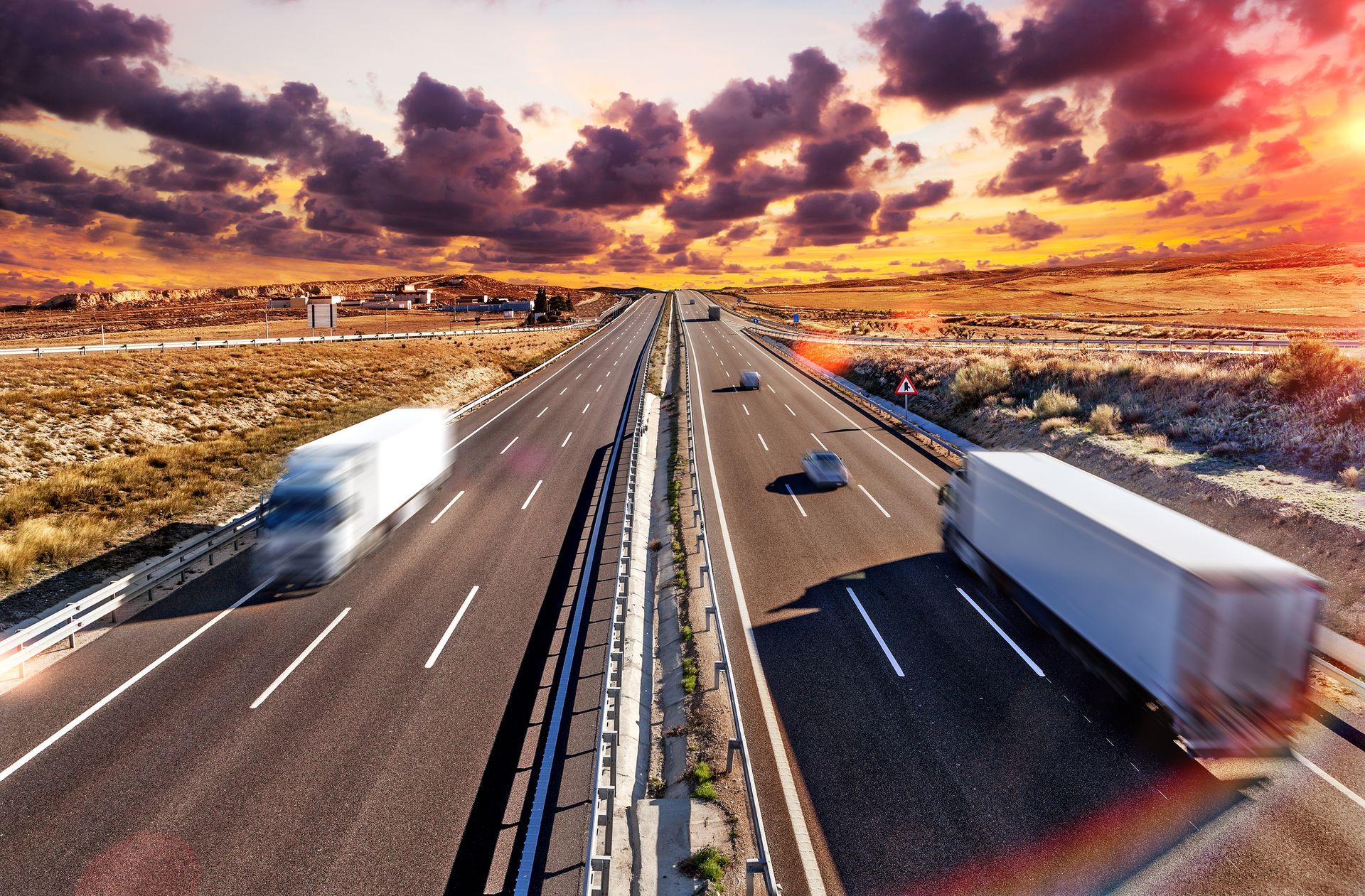 Highway with semi-trucks under dramatic sunset sky.