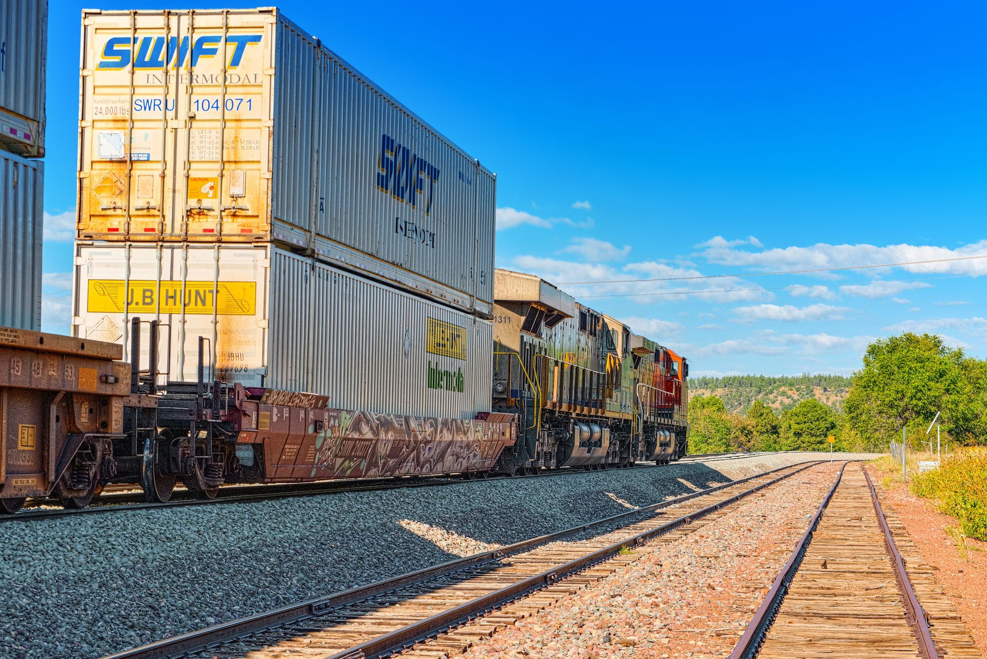 Train with Swift shipping containers on tracks, against a blue sky.