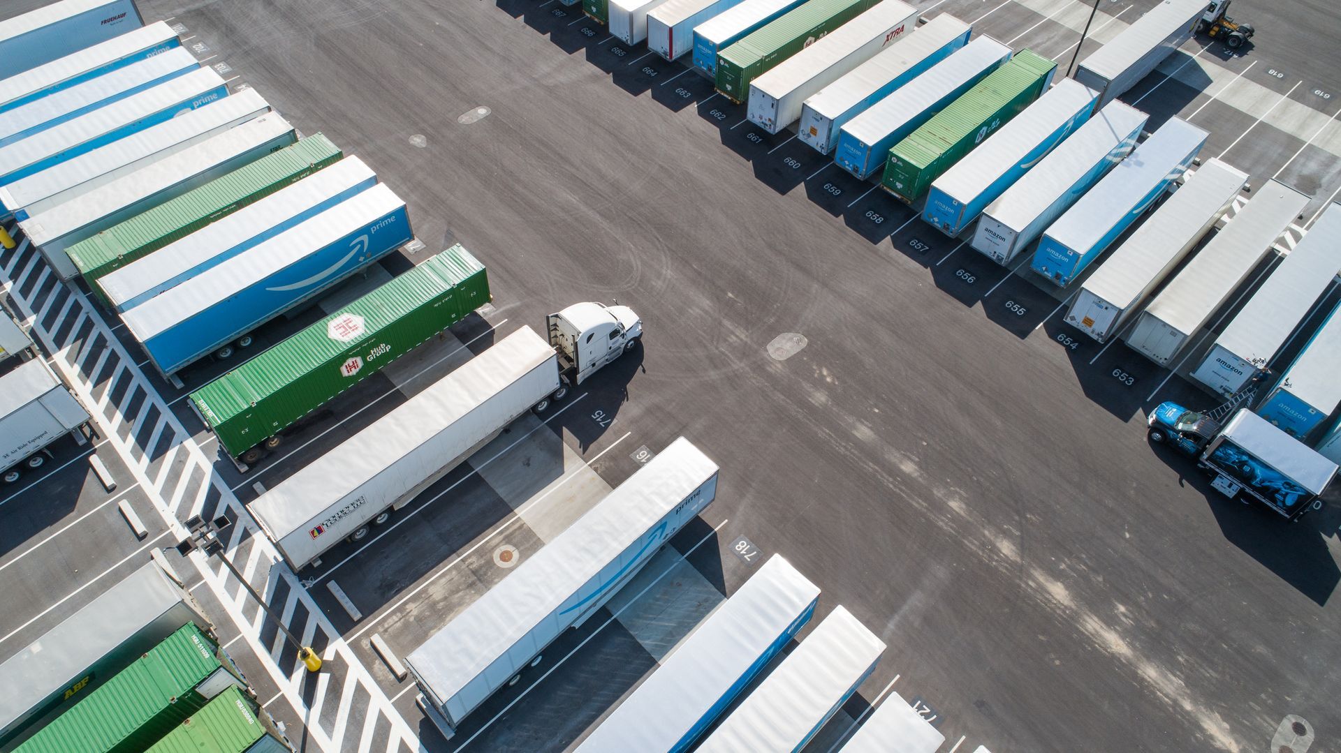 Overhead view of a truck pulling out of a busy truck stop; trailers are parked in rows.