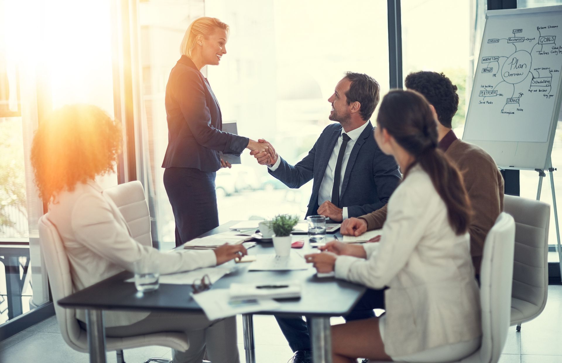 Businesspeople in a bright conference room, shaking hands to seal a deal.