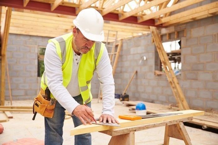 Carpenter in a safety vest measuring lumber at a construction site.