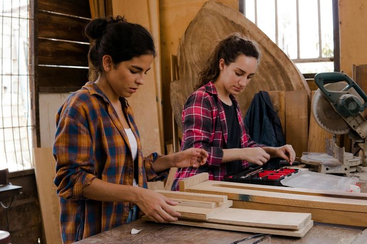 Two women working together on a woodworking project in a shop.