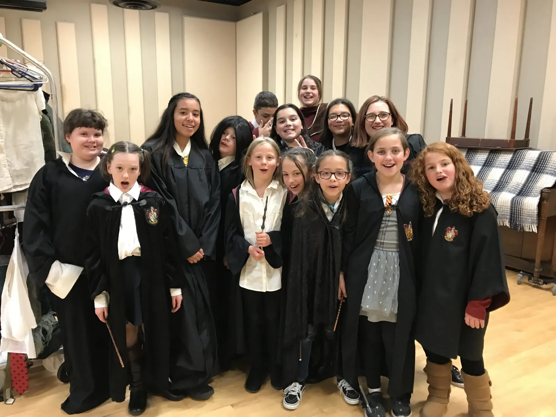 Group of kids in Hogwarts robes, posing with wands indoors.