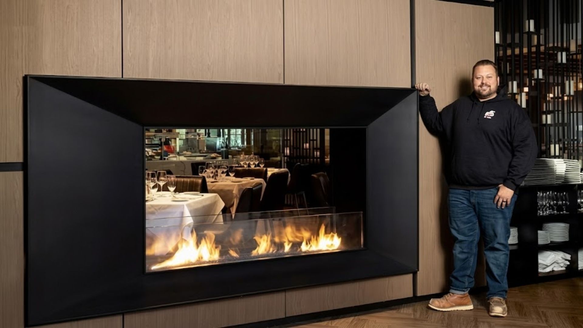 Modern black fireplace in a wood-paneled room, with a man standing beside it.