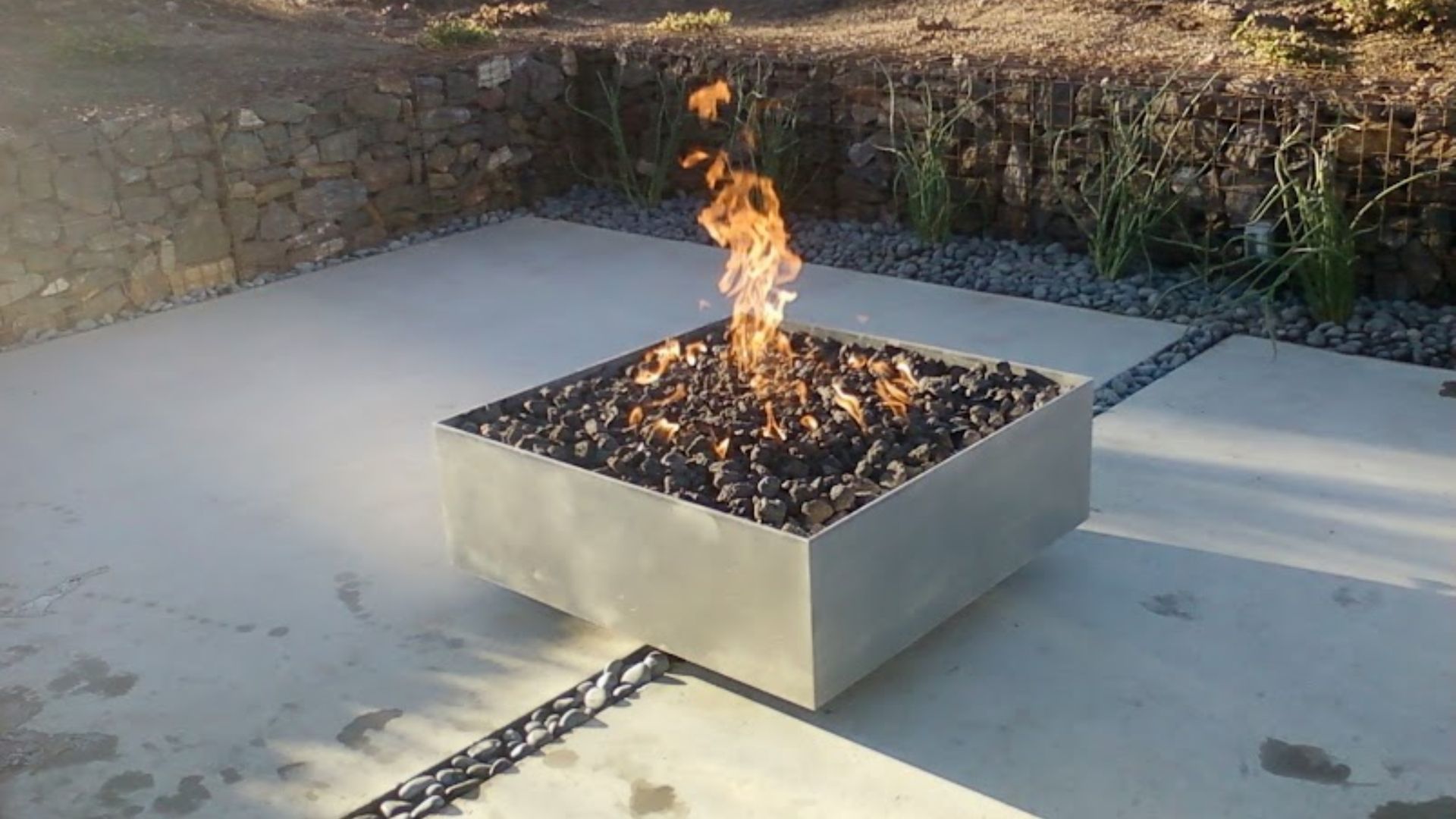 Outdoor square fire pit with burning flames on a concrete patio