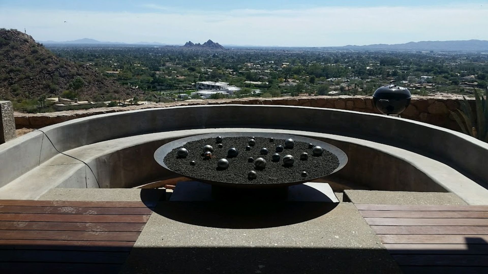 Panoramic city view from a curved stone overlook with a circular bench in the foreground