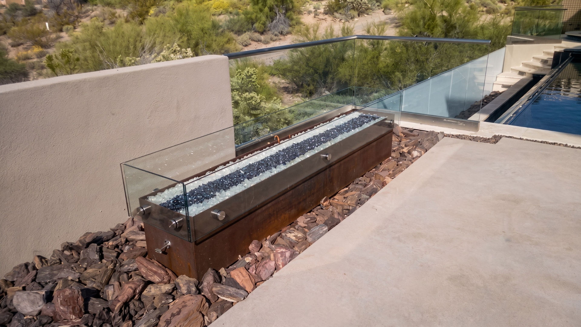 Outdoor upright piano beside a water feature, set on rocks near a concrete walkway.