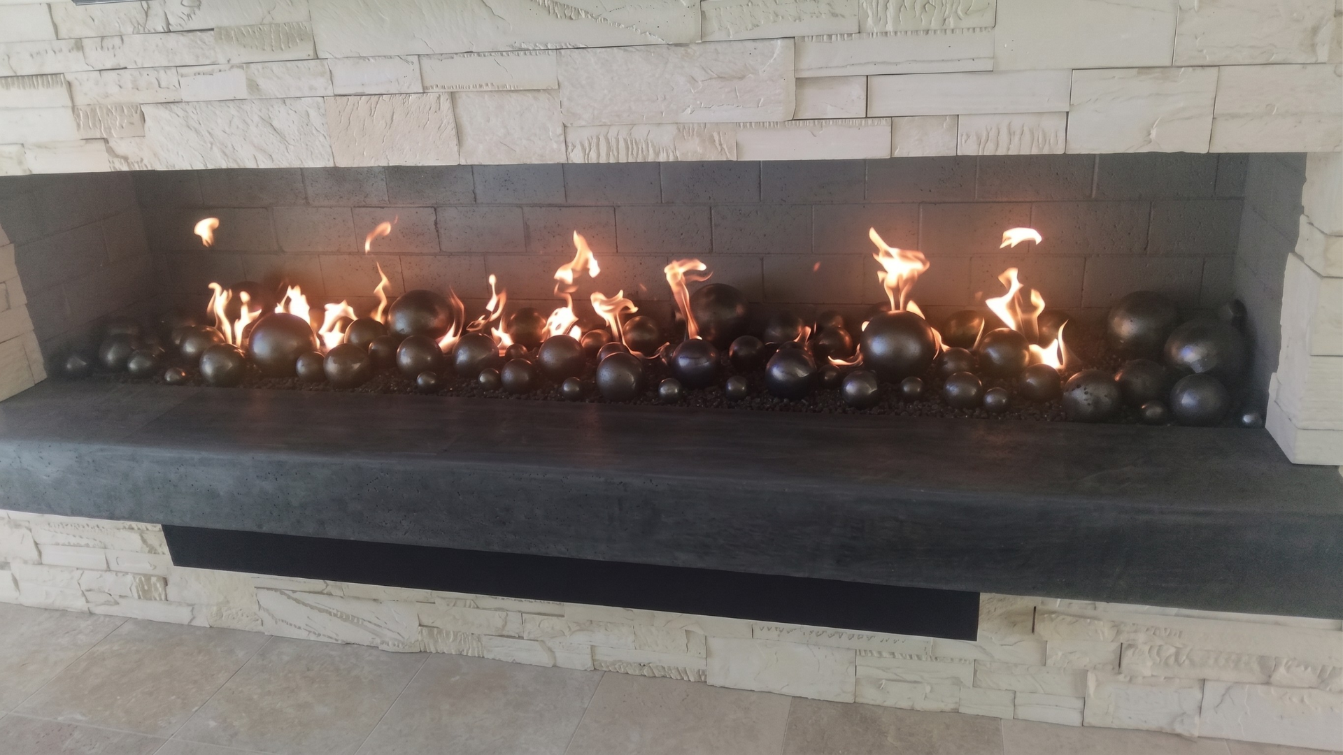 Modern indoor gas fireplace with flames above black stones set in a stone surround