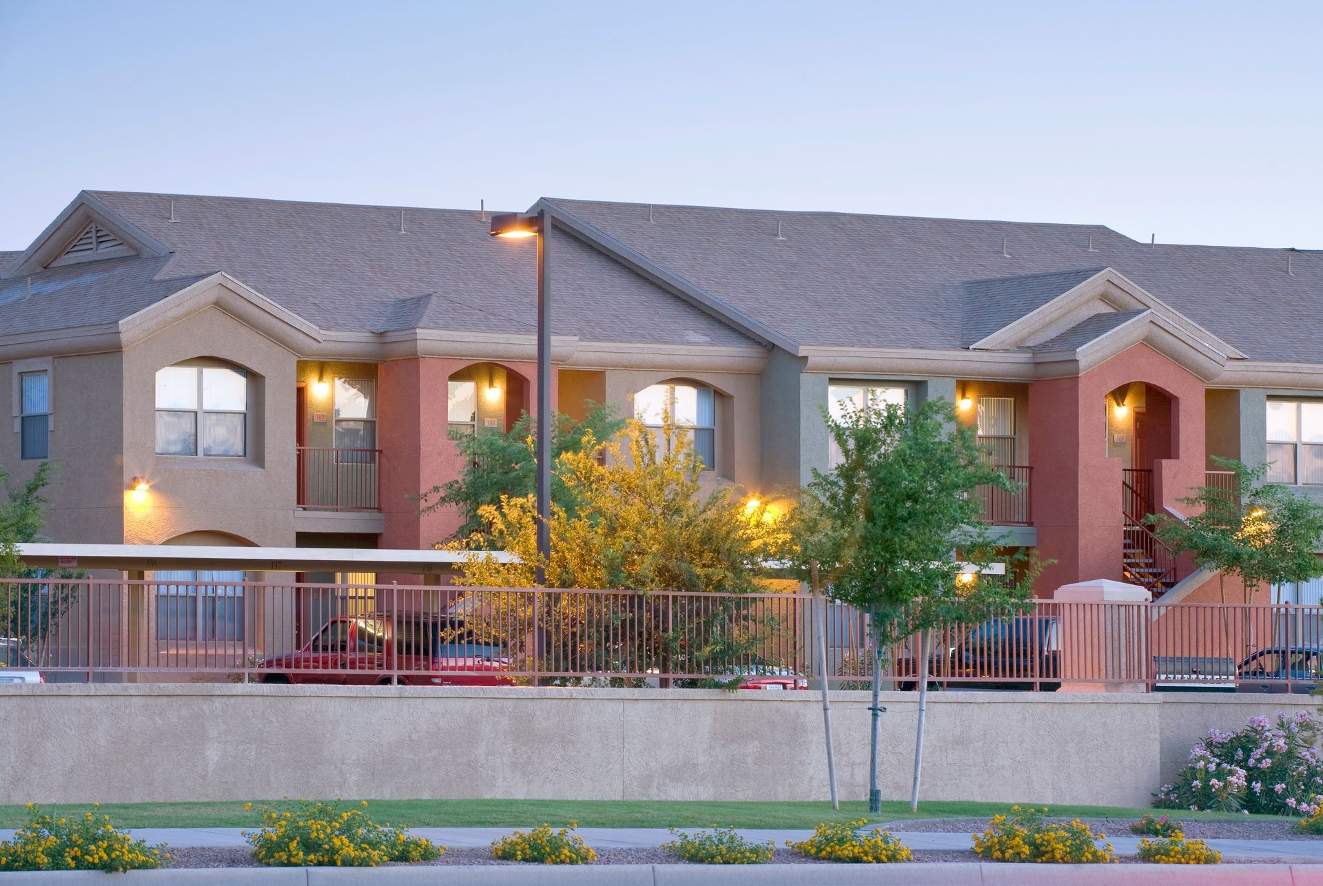 A multi-story apartment building with tan and reddish-brown stucco walls, a grey shingled roof, and a low front wall.