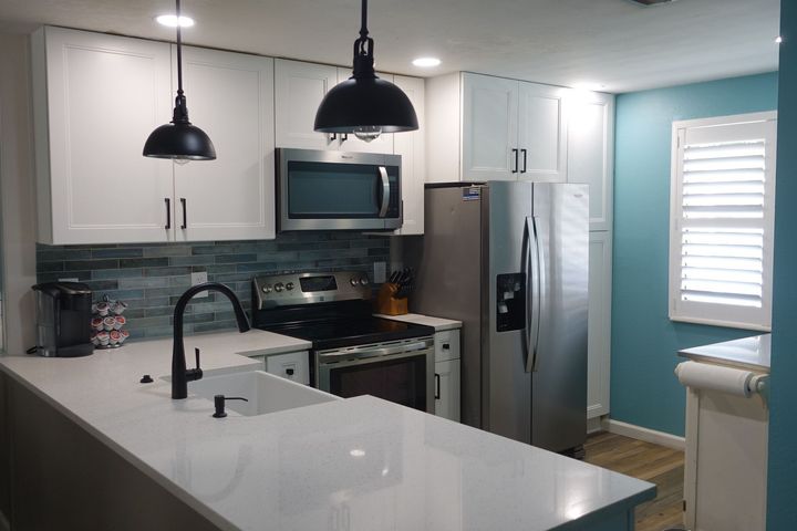Modern kitchen with white island, black pendant lights, stainless appliances, and teal accent wall