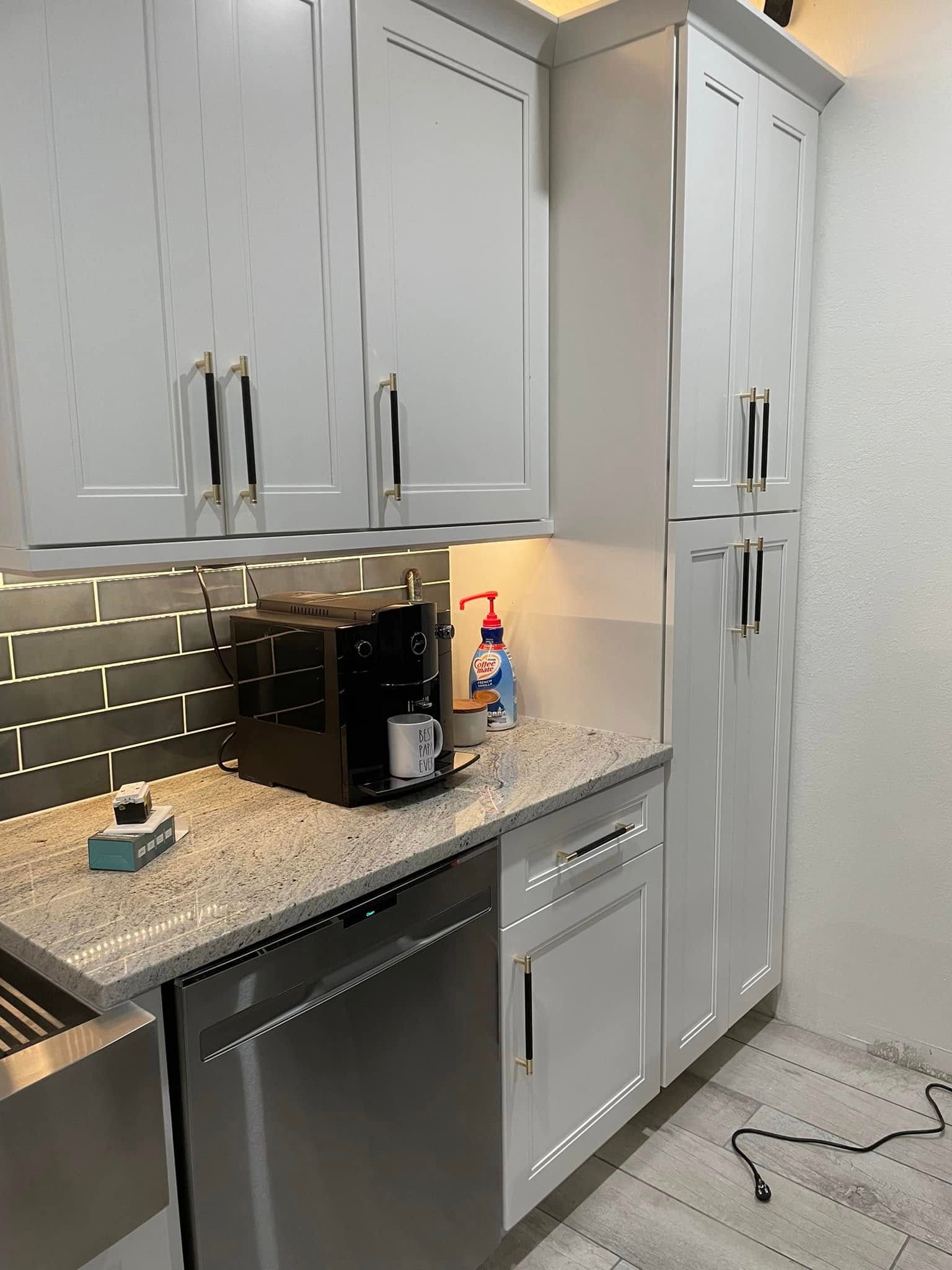 Modern kitchen with gray cabinets, speckled countertop, black coffee maker, and tiled backsplash