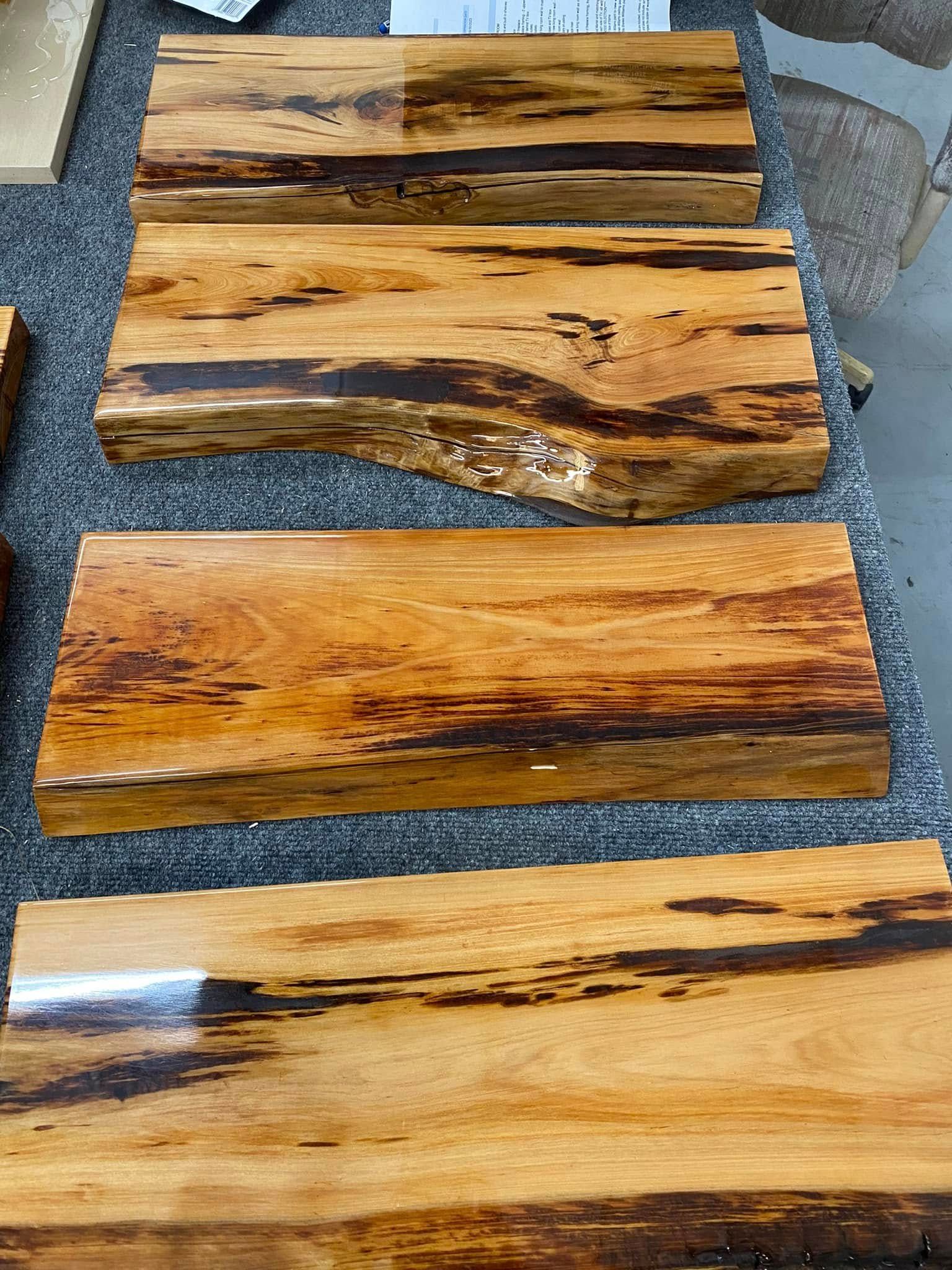 Four polished live-edge wooden slabs with dark grain, laid on a textured gray surface.