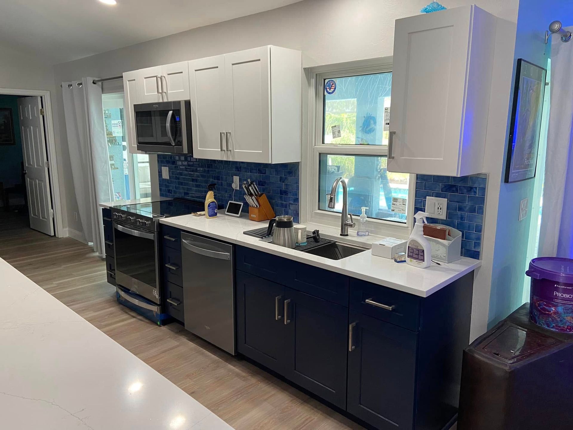 Modern kitchen with white and navy cabinets, stainless appliances, and a bright window over the sink