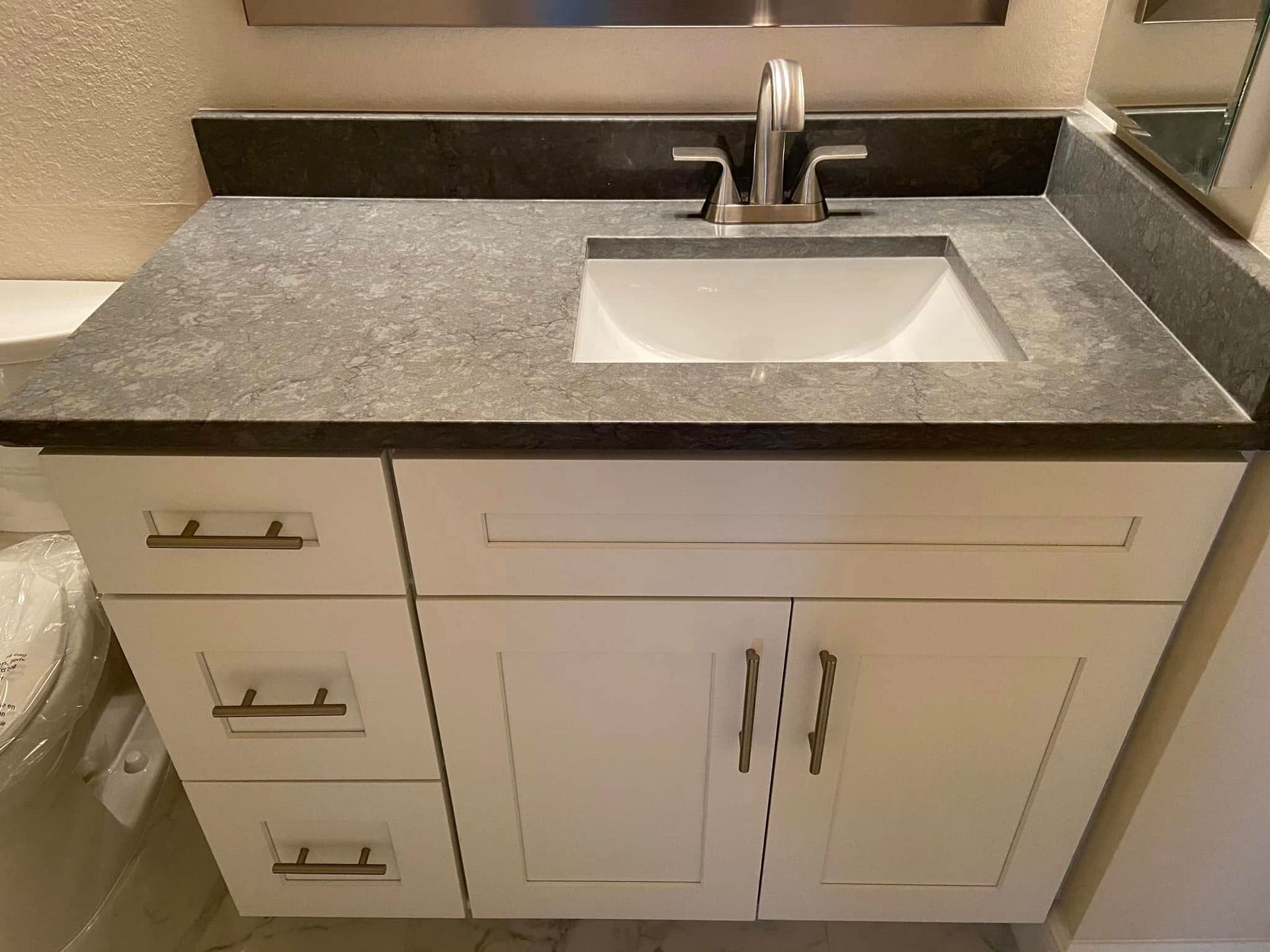 Bathroom vanity with gray countertop, white cabinets, and single sink under a mirror.