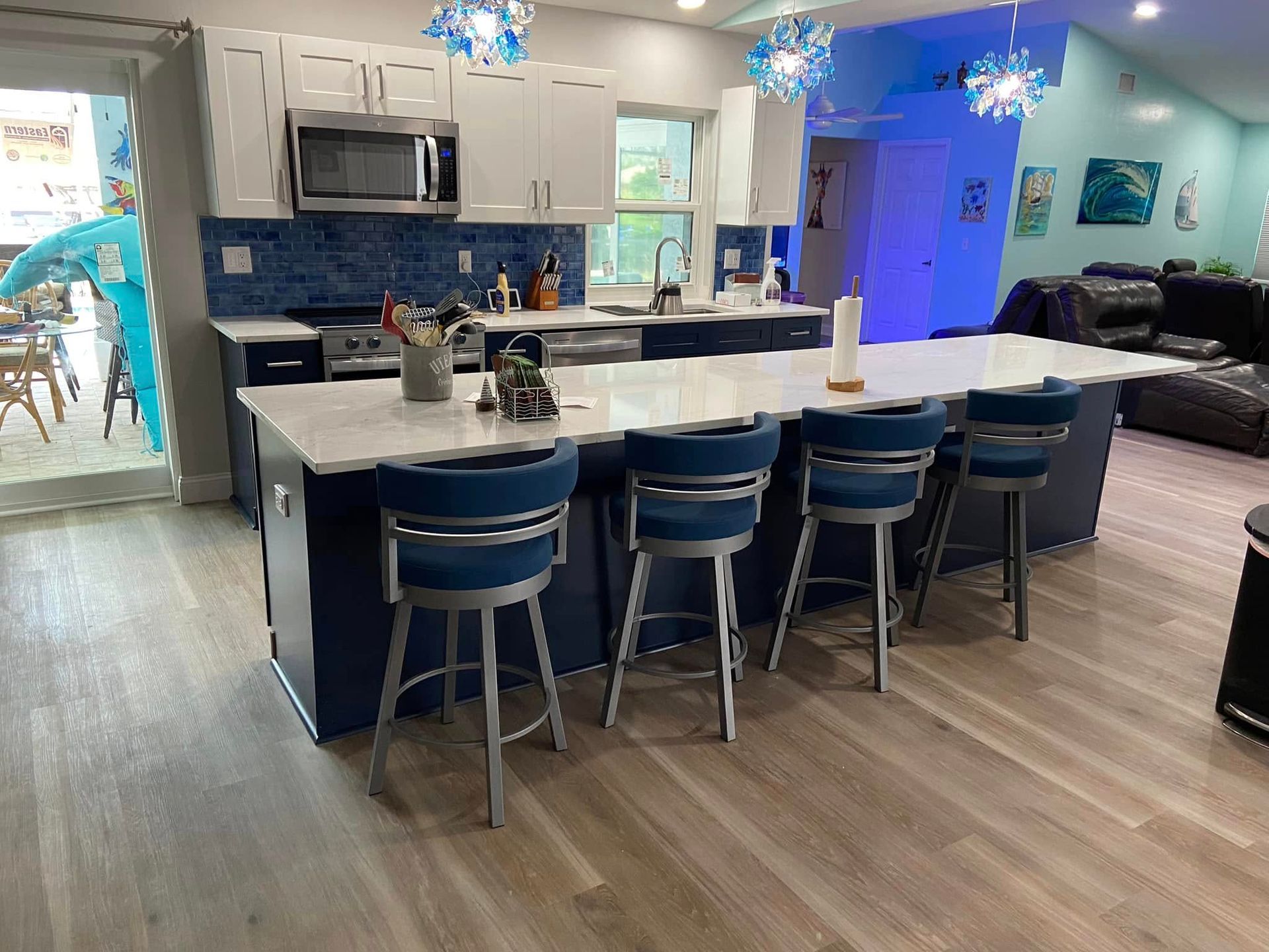 Bright modern kitchen with blue island stools, gray cabinets, and open living area with blue decor