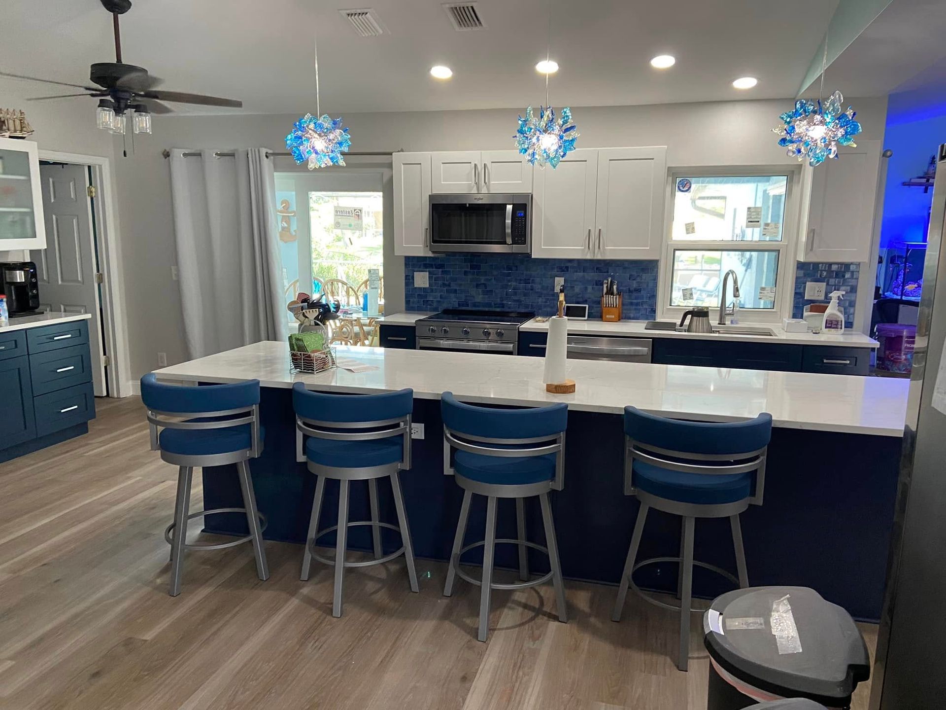 Modern kitchen with white island, blue bar stools, pendant lights, and stainless steel appliances
