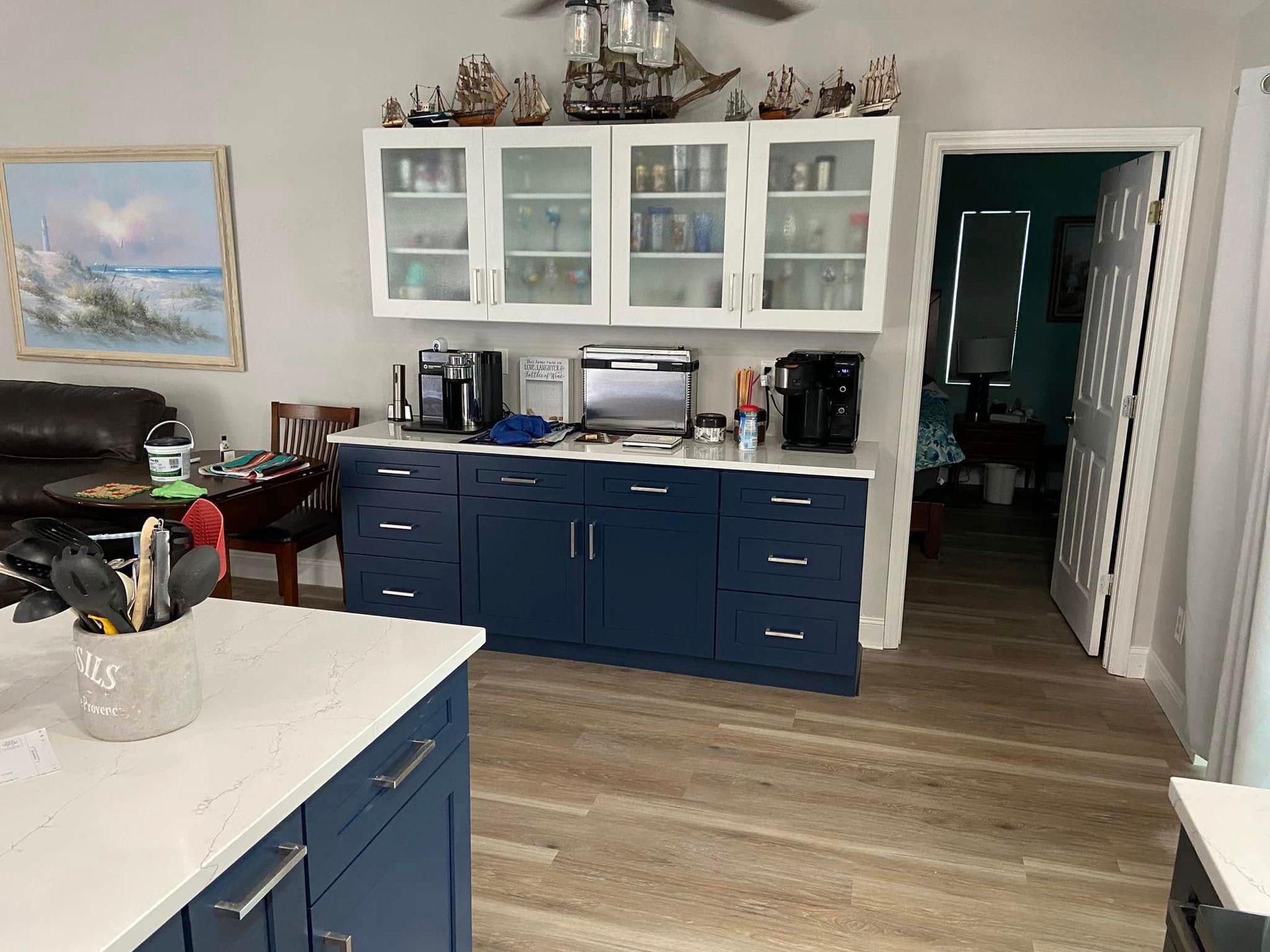 Bright kitchen with blue cabinets, white countertops, and a doorway to a dim hallway