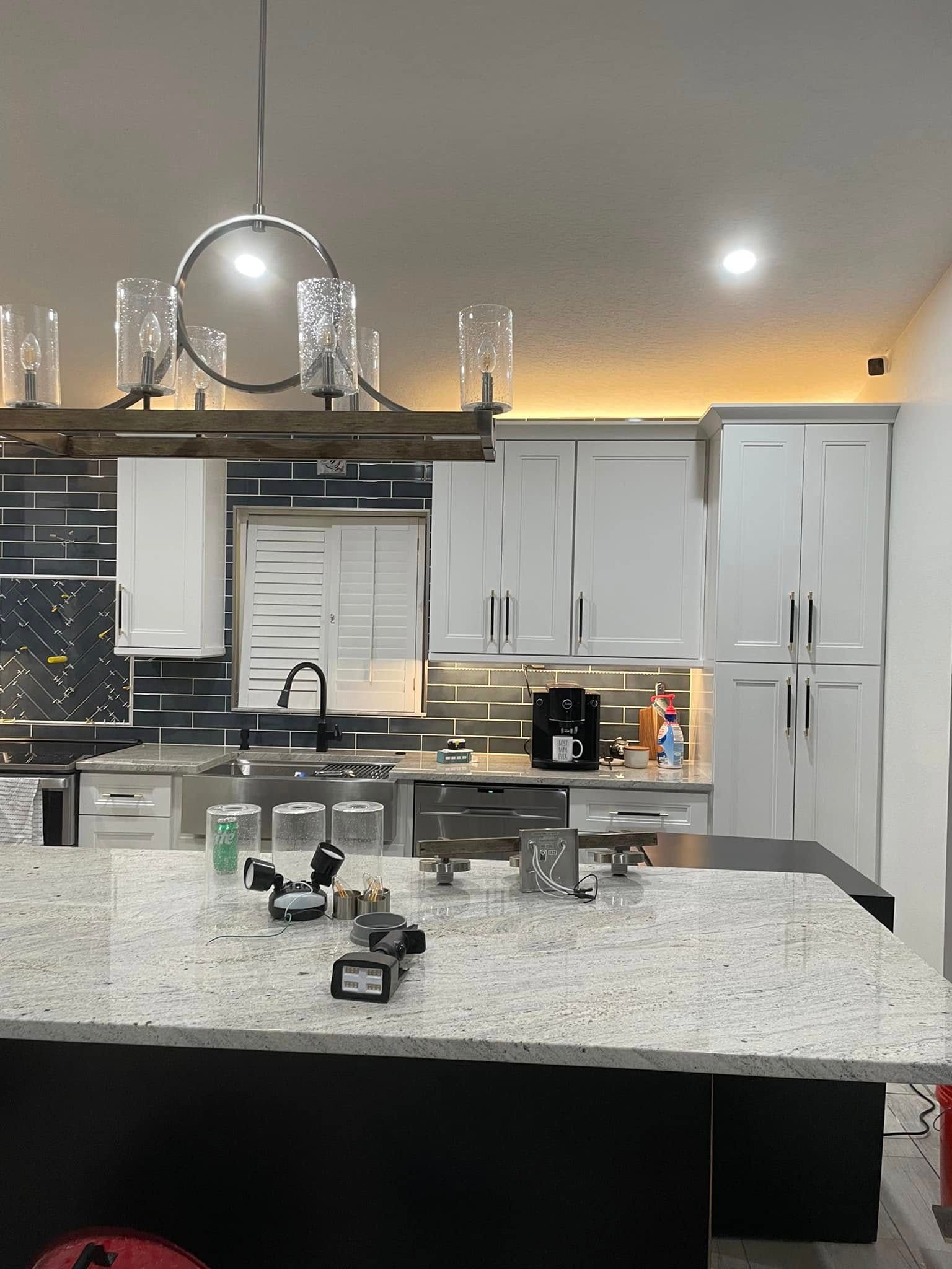 Modern kitchen with granite island, gray cabinets, and a city skyline visible through the window.