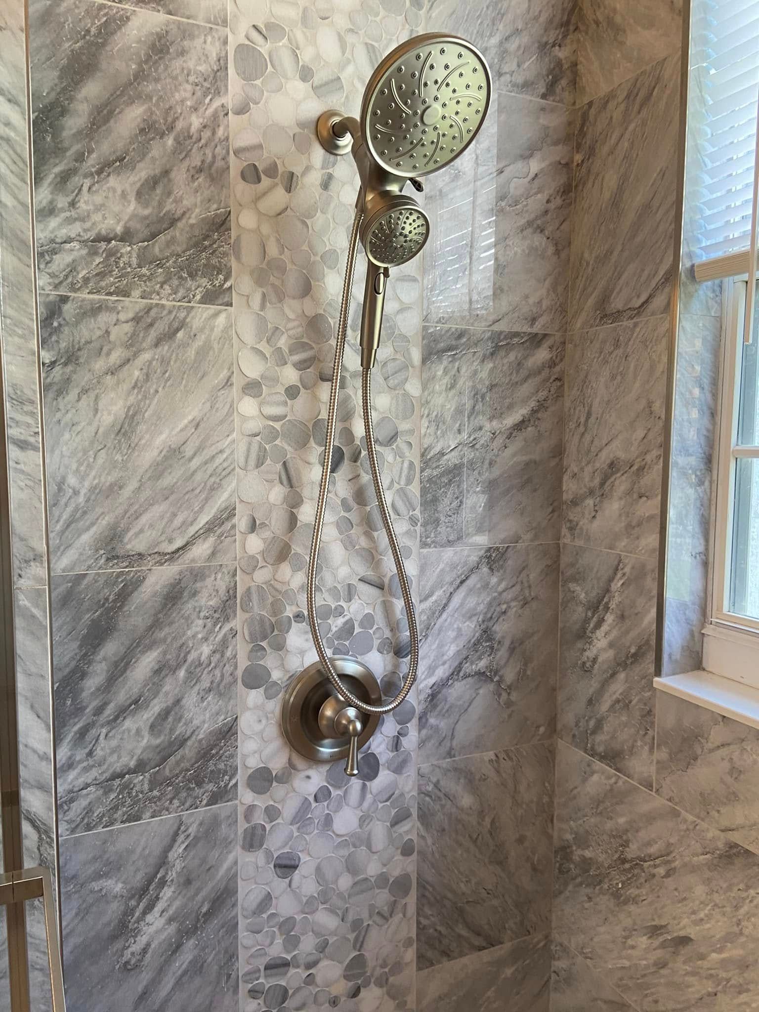Handheld showerhead with long hose mounted on a tiled bathroom wall near a window