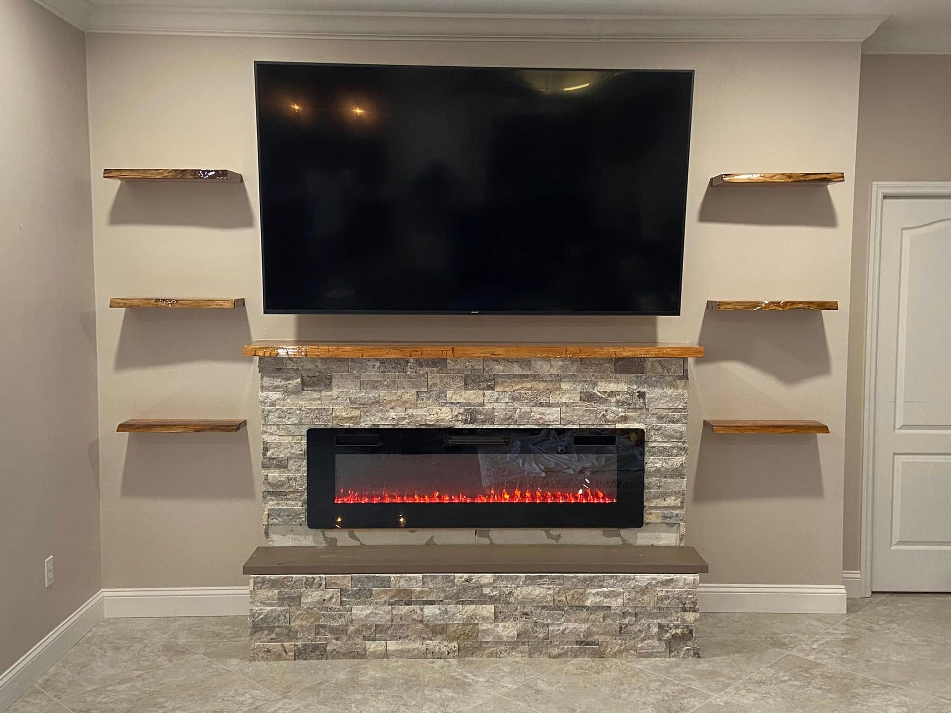 Living room wall with mounted TV above a stone fireplace and floating shelves on both sides