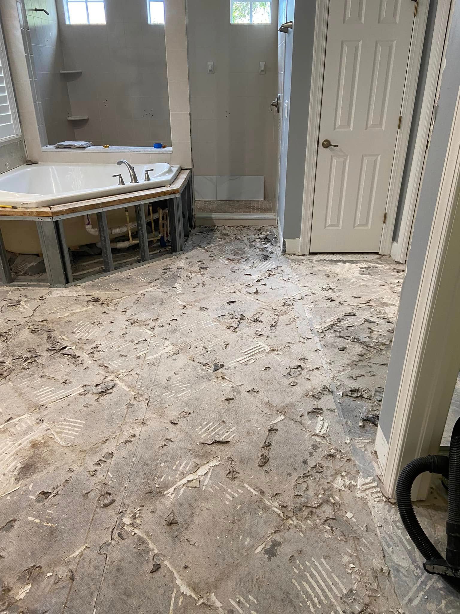 Bathroom floor covered in debris and dust beside a bathtub and open door