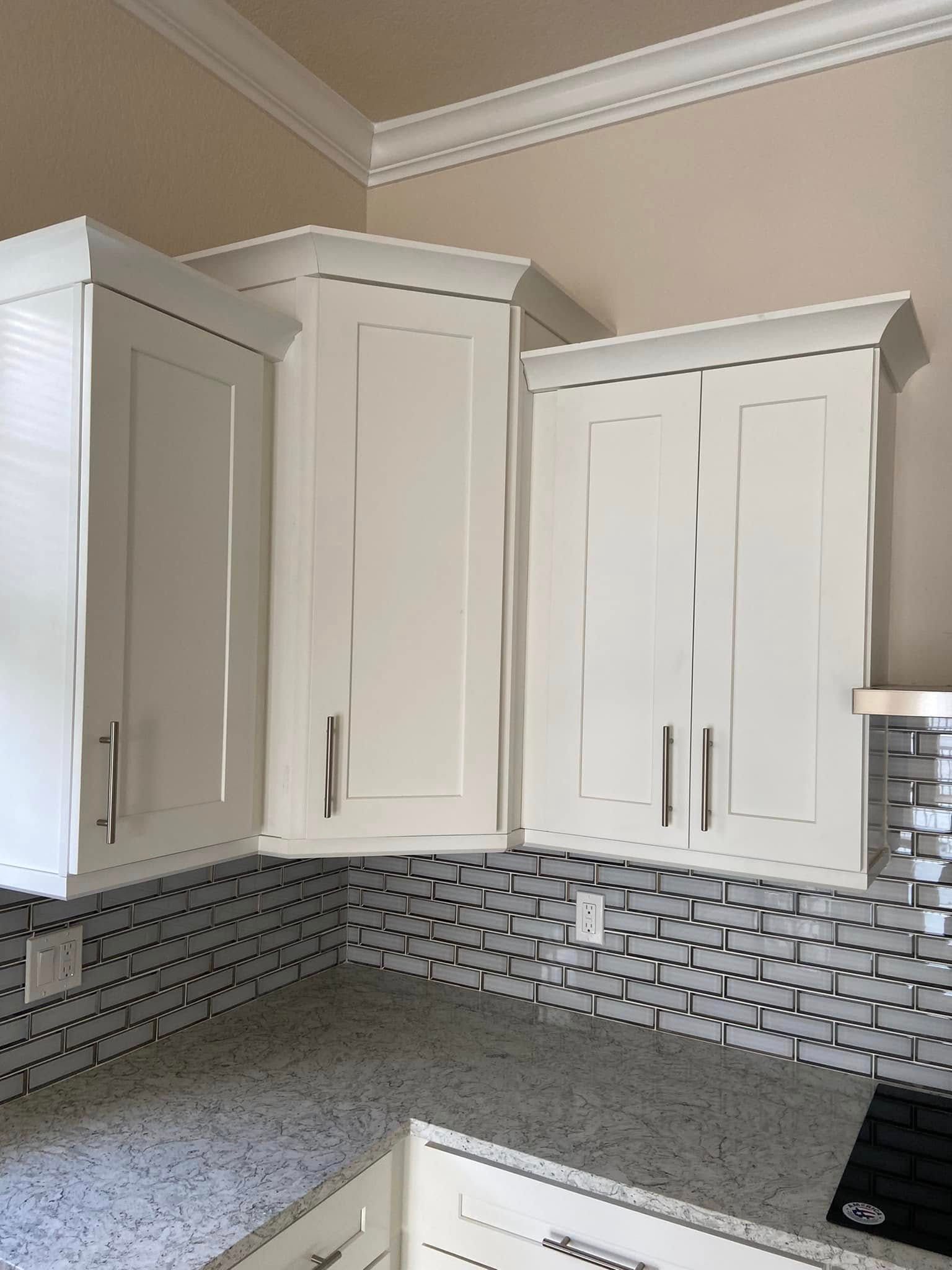 White kitchen cabinets above a gray mosaic tile backsplash and speckled countertop