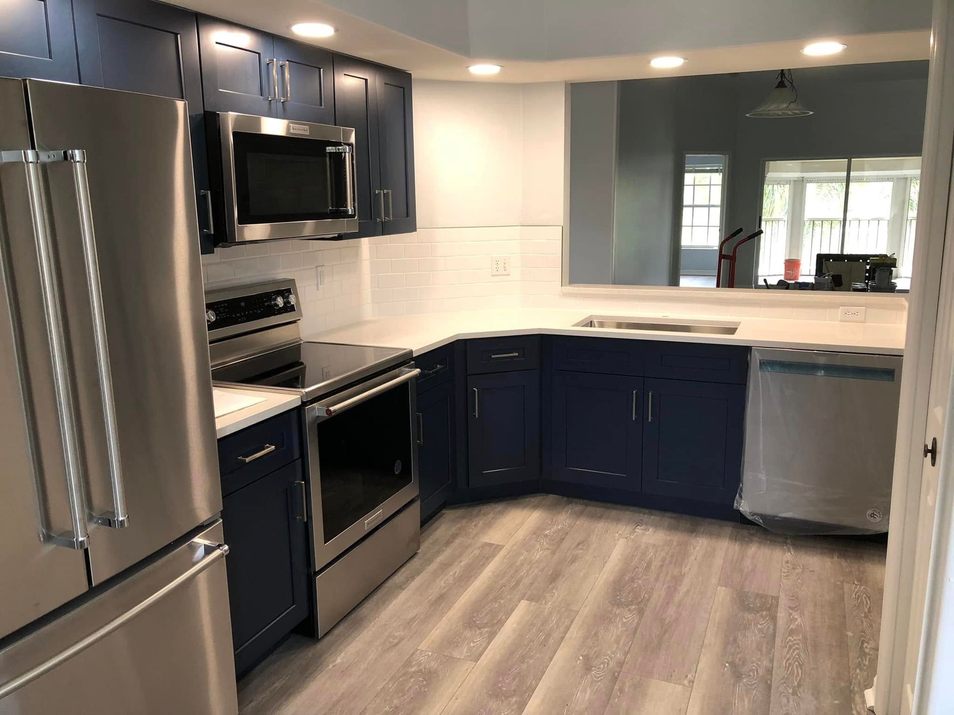 Modern kitchen with dark blue cabinets, stainless steel appliances, and light wood flooring