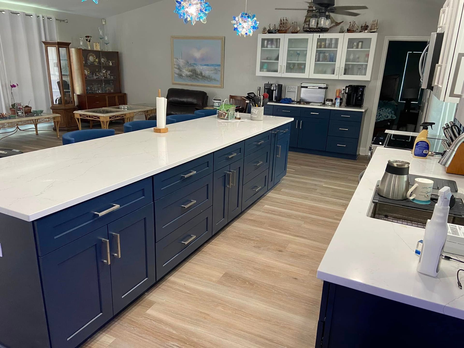Modern kitchen with white island countertops, navy cabinets, light wood floors, and blue pendant lights