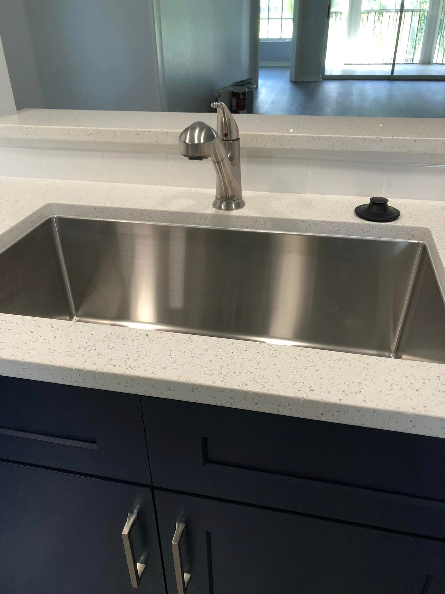 Stainless steel kitchen sink with black countertop and dark cabinets underneath.