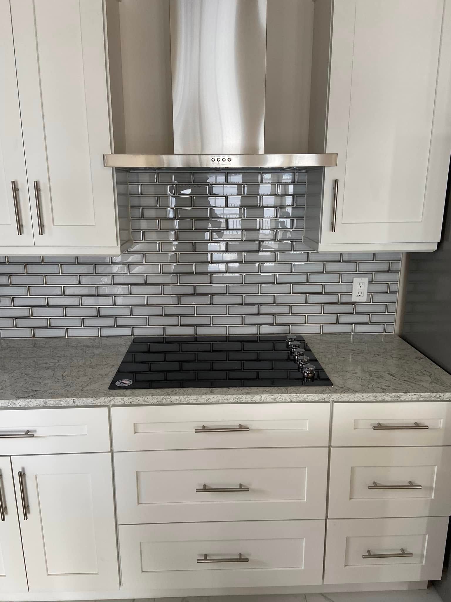 Modern kitchen with white cabinets, gray tile backsplash, black countertop, and stainless range hood