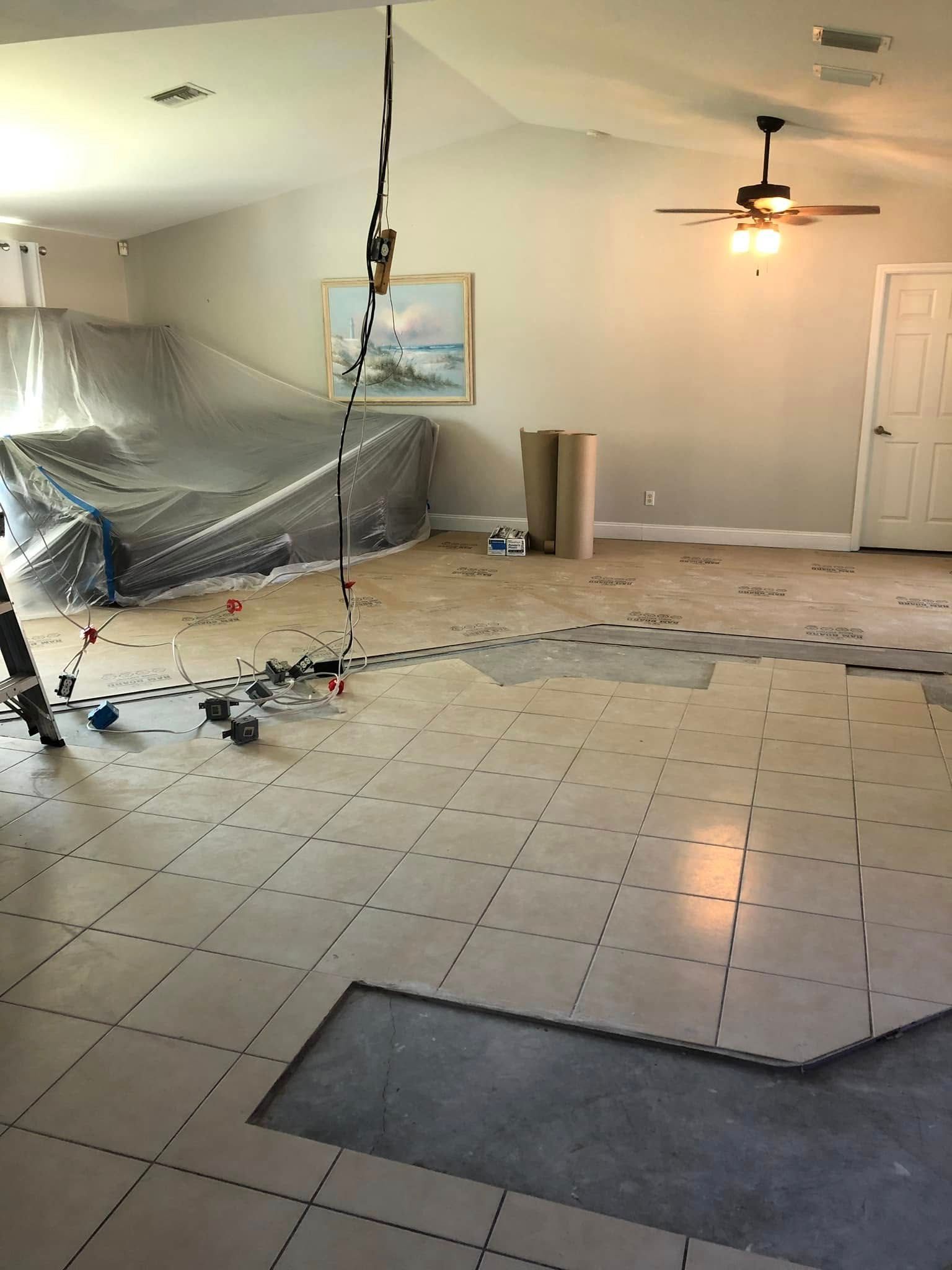 Damaged living room with torn ceiling plastic, scattered debris, and overturned furniture on tiled floor.